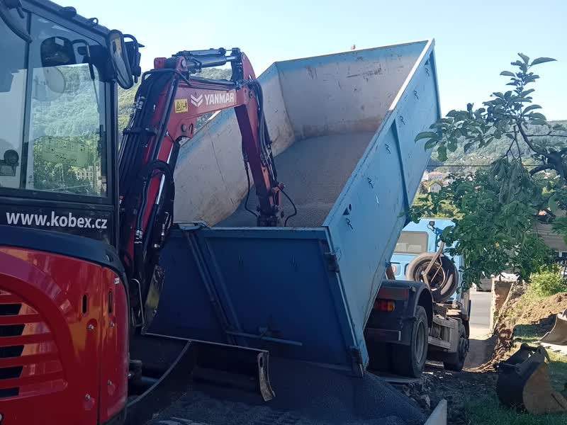 Minibagr nakládá výkopek do kontejneru na sklápěči